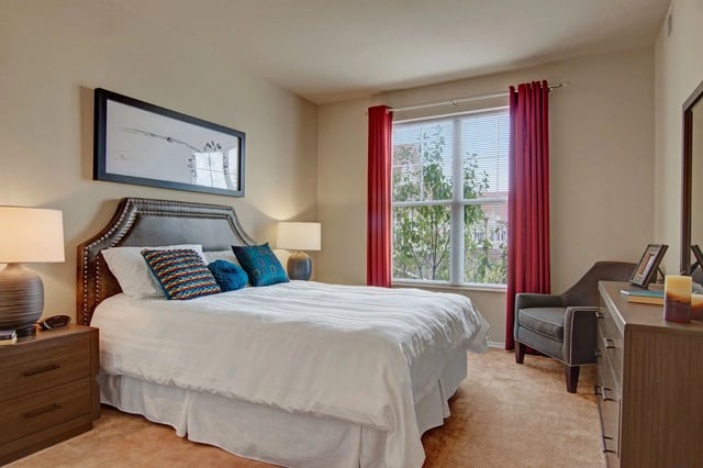 Bedroom with a large bed, nightstands, and a window with red curtains.