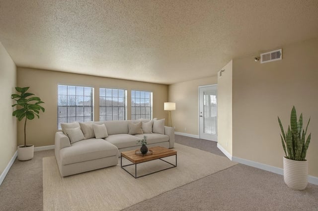 Living room with sectional sofa, coffee table, large windows, and a door leading outside.