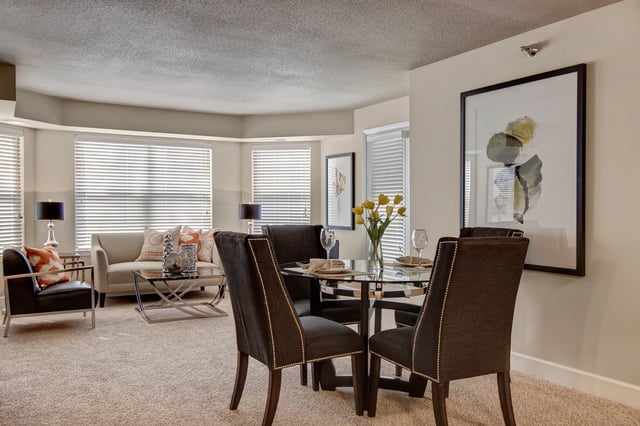 Dining area and living room with modern furniture, including a glass-top table with chairs and a sofa by the window.