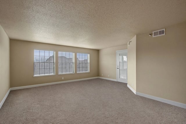 Spacious living room with neutral carpet, three large windows, and a glass door.