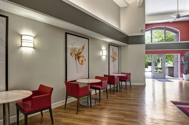 Lobby area with modern red chairs and tables, artwork on walls, and entrance visible.