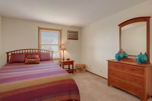 Bedroom with a queen-size bed, dresser with mirror, and a window with blinds.