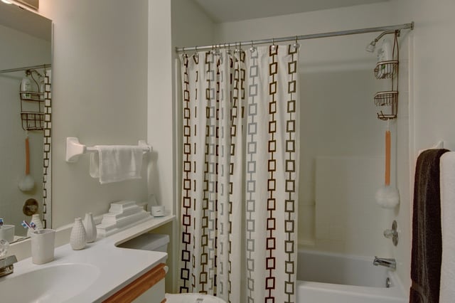 Clean, modern bathroom with a white vanity, mirror, and bathtub with a patterned shower curtain.