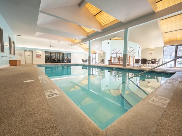 Indoor swimming pool with lounge chairs and tables.