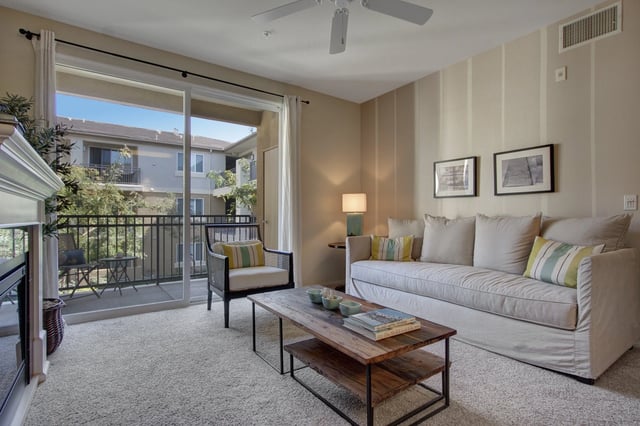 Living room with sofa, coffee table, armchair, and balcony access.