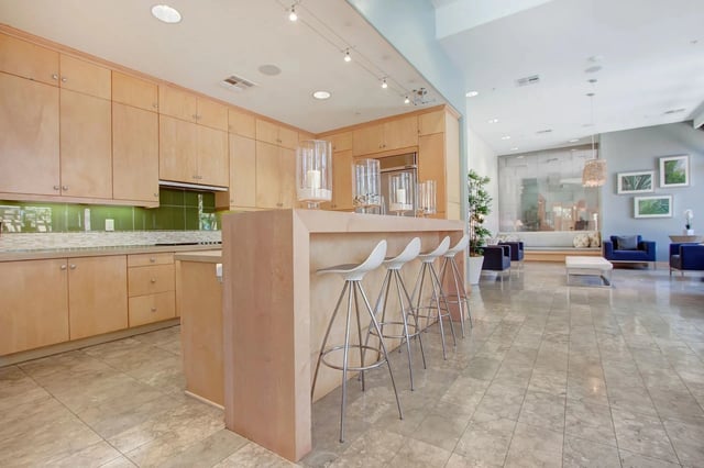 Modern kitchen with light wood cabinets, granite countertops, and a breakfast bar with white stools.