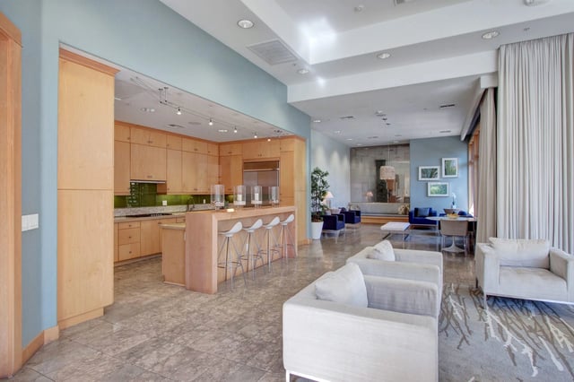 Modern kitchen with wood cabinets and island with bar stools, open to a spacious living area with white sofas and a dining table.