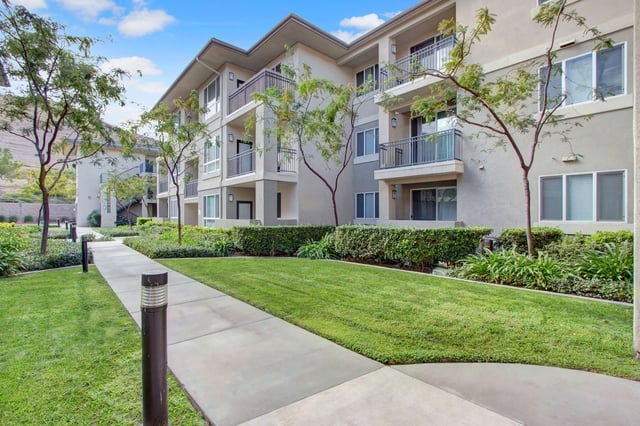 Exterior view of apartment buildings with a walkway and manicured landscaping.