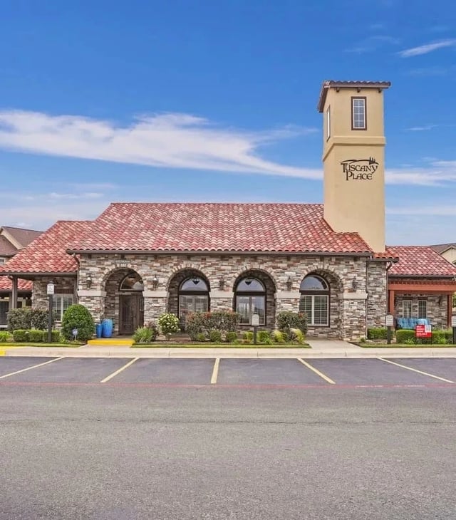 Exterior view of Tuscany Place apartment community with stone facade and red-tile roof.