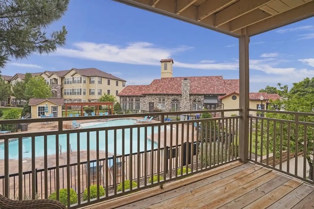 View from a balcony overlooking a resort-style apartment pool with lounge chairs and surrounding buildings.