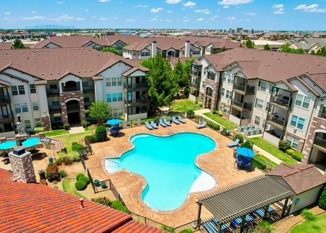 Outdoor pool at a residential apartment complex with lounge chairs and red-tile surrounding area.
