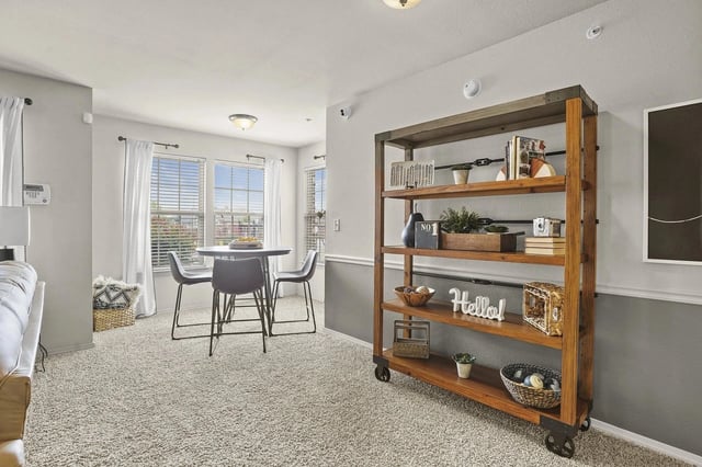 Modern apartment living area with round dining table near windows and a wooden rolling shelf.
