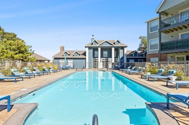 Outdoor apartment pool with lounge chairs and a central clubhouse in the background.