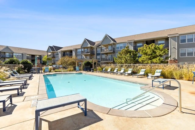 Outdoor community pool surrounded by lounge chairs with apartment buildings in the background.