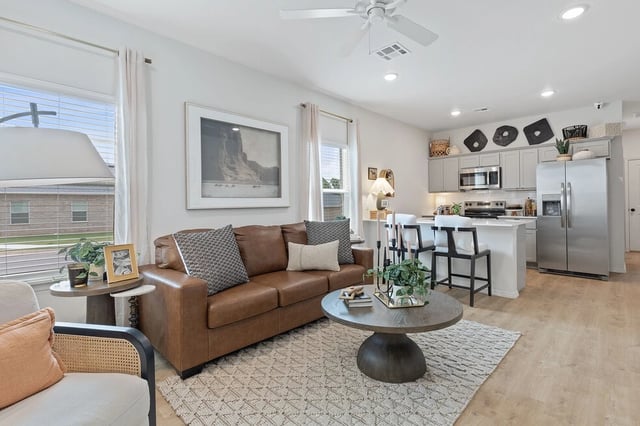 Living room and kitchen of an apartment with a brown leather sofa, coffee table, and island.
