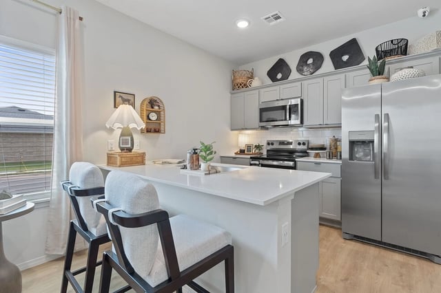Modern kitchen with a large island, stainless steel appliances, and light gray cabinets.