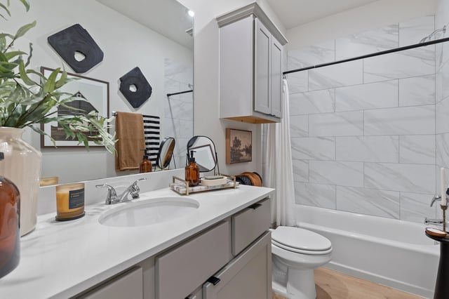 Modern bathroom with a vanity, toilet, and bathtub with white marble tile.