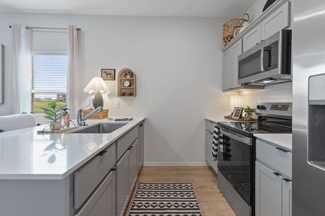 Modern kitchen with light gray cabinets, white quartz countertops, stainless steel appliances, and a large sink.
