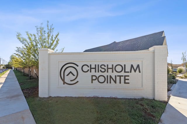 White brick community entrance sign reading 'Chisholm Pointe' with trees and sidewalk.