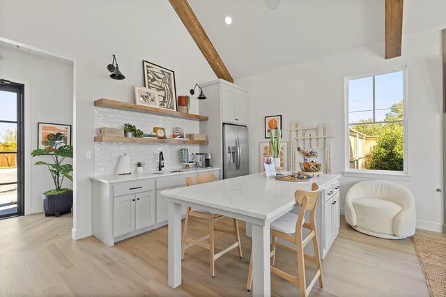 Bright modern kitchen with white cabinets, island, open shelves, and a large window.