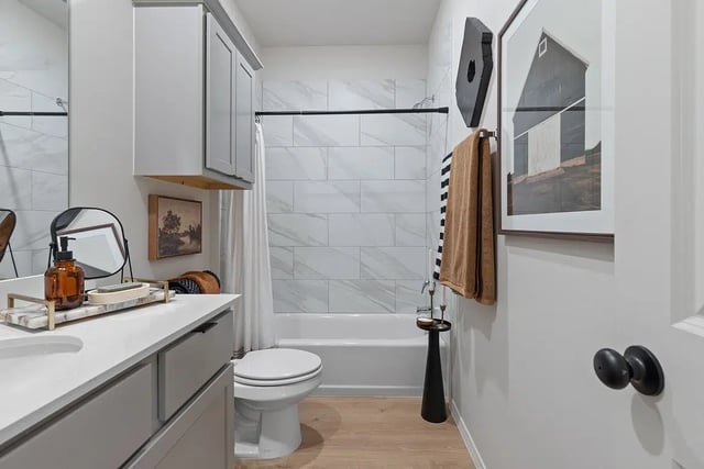 Modern gray bathroom with vanity, toilet, and tiled tub surround.