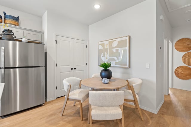 Dining area with round table, four chairs, and a stainless steel refrigerator nearby.