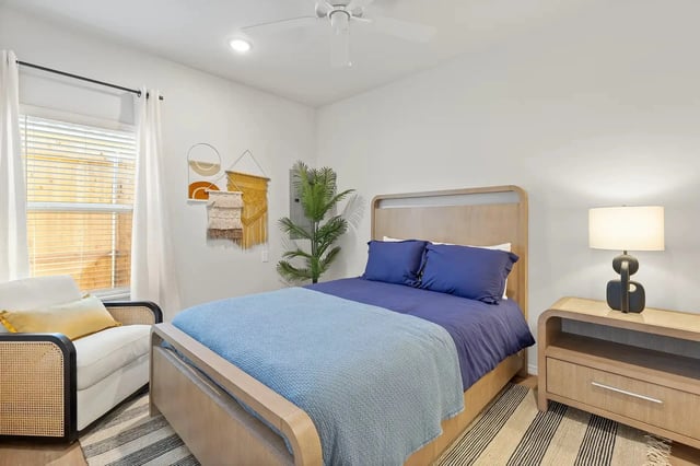Bedroom in a modern apartment with a wooden bed, blue bedding, lamp, and plants.