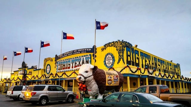 Exterior view of The Big Texan Steak Ranch, a bright yellow building with Texas flags and a large steer statue.