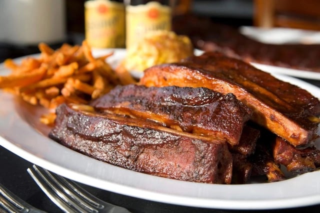 Close-up of sliced smoked barbecue ribs with fries on a white plate.