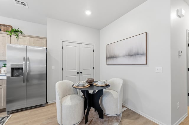 Dining area with a round table and two chairs in front of a stainless steel refrigerator and white double doors.