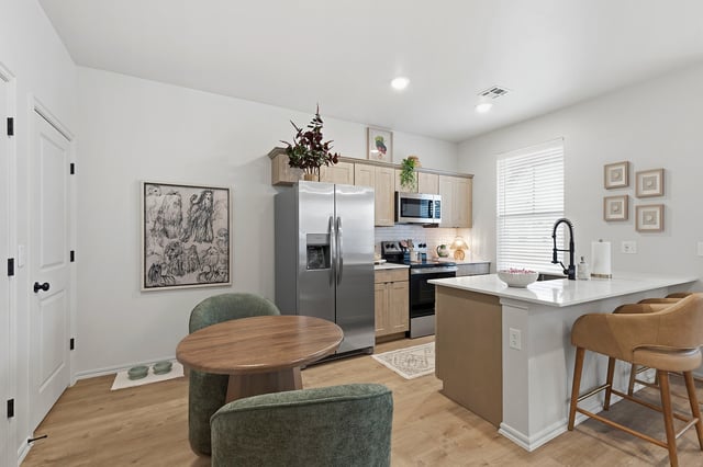 Modern kitchen with stainless steel appliances, a breakfast bar with bar stools, and a small dining table.