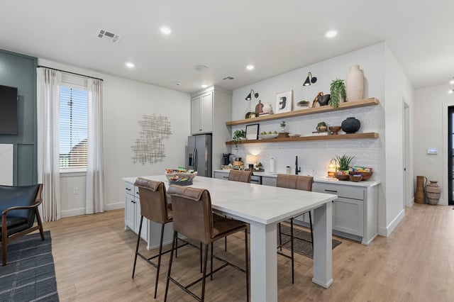 Modern kitchen with island and bar stools, featuring stainless steel appliances and open shelving.