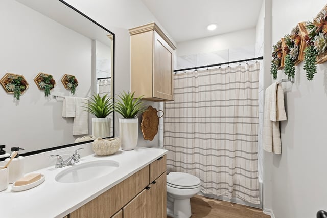 Modern bathroom with wood-grain vanity, white countertop, sink, toilet, and striped shower curtain.