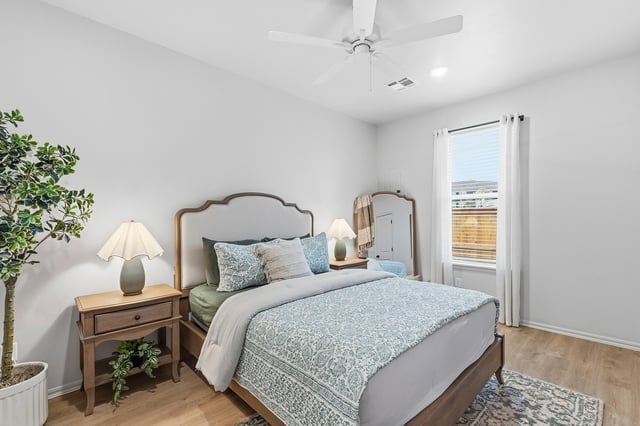 A cozy bedroom with a king-sized bed, nightstand, lamp, ceiling fan, and a large window.