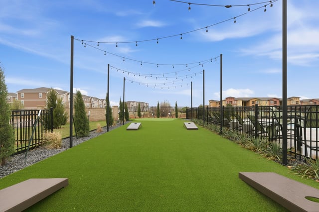 Outdoor lawn games area with cornhole boards and string lights.