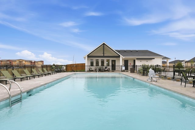 Outdoor swimming pool with lounge chairs and a building in the background.