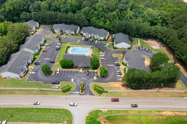 Aerial view of apartment complex with a pool, playground, and parking lots.