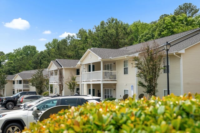 Exterior view of apartment buildings with parked cars and lush green foliage.