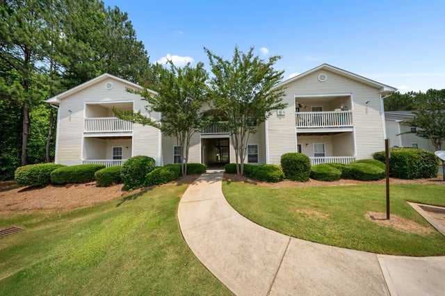 Exterior view of apartment building with manicured landscaping and a curved walkway.