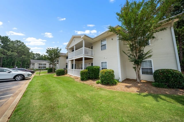 Exterior view of a cream-colored apartment building with a balcony and green lawn.