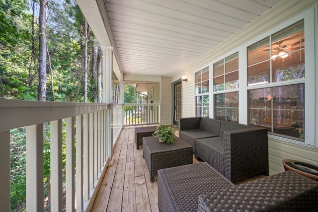 Covered balcony with wicker furniture overlooking wooded area.