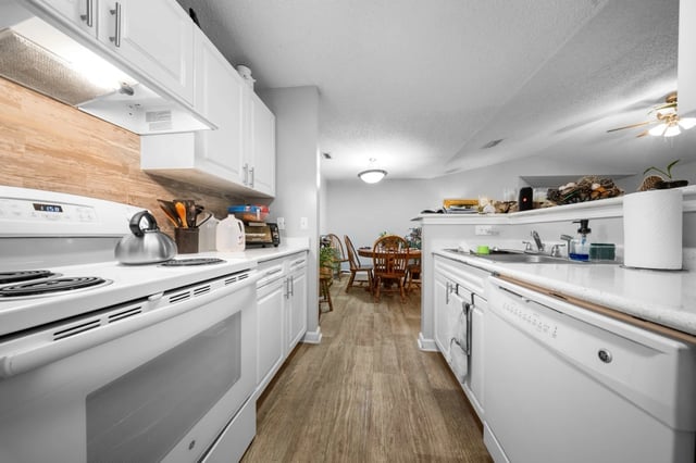 Modern white kitchen with wood-look flooring and stainless steel appliances.