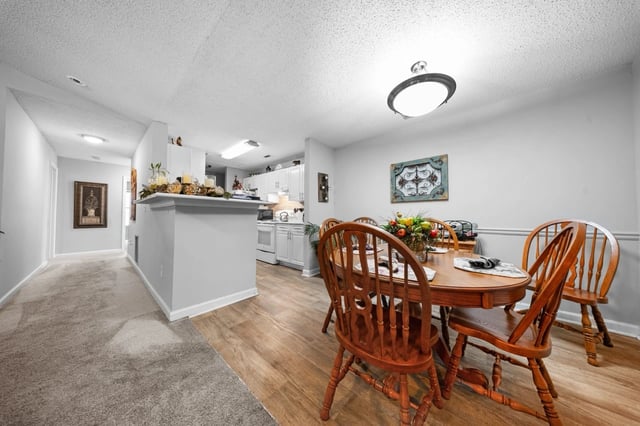 Dining area with a round wooden table and chairs, adjacent to a kitchen.