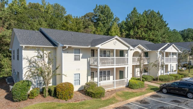 Exterior view of a multi-story apartment building with balconies and surrounding green landscaping.