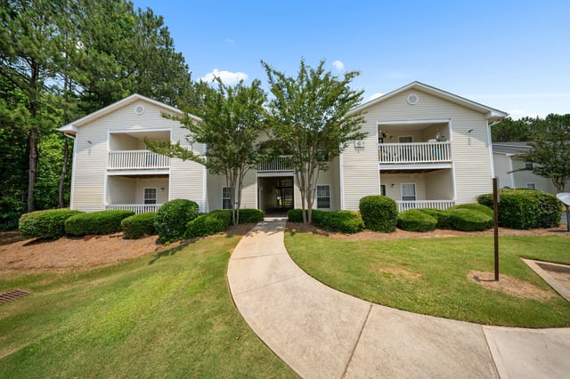 Exterior view of apartment buildings with a paved walkway leading to the entrance at Ashton Pointe apartments in Monroe, GA.