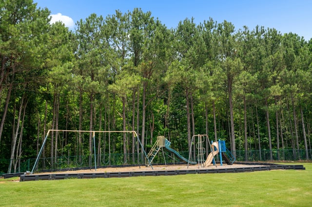 Playground with swings and slides next to a dense forest at Ashton Pointe apartments in Monroe, GA.