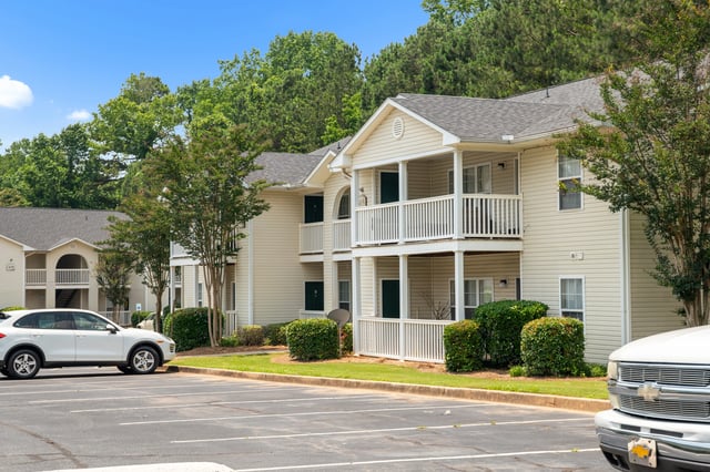 Exterior view of apartment buildings with a parking lot and cars at Ashton Pointe apartments in Monroe, GA.