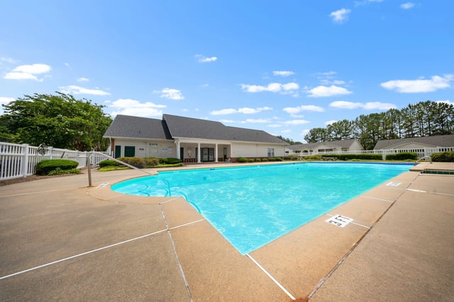Sparkling outdoor swimming pool with a large deck area and building in the background at Ashton Pointe apartments in Monroe, GA.