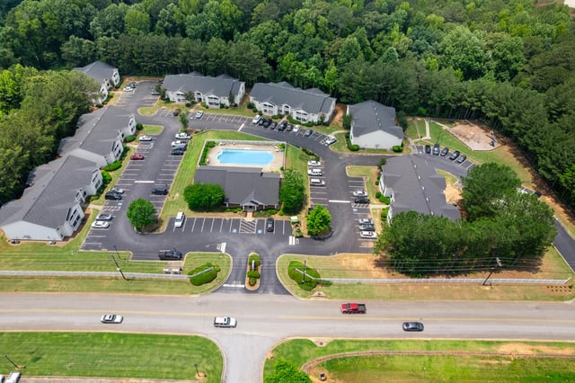 Aerial view of a multifamily property with apartment buildings, a swimming pool, and a playground at Ashton Pointe apartments in Monroe, GA.