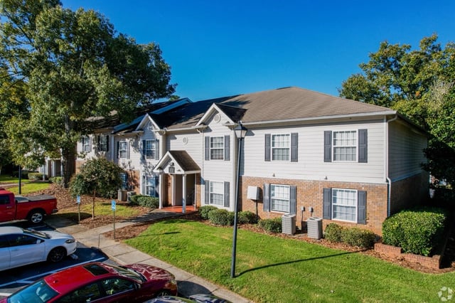 Exterior view of apartment buildings with trees and parking lot.